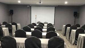 A conference room with rows of tables and chairs, a projector screen, and speakers.