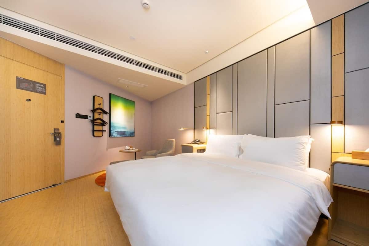 A hotel room with a large bed, a chair, a small table, and a wall-mounted artwork.