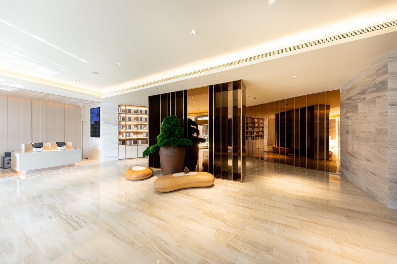 A modern lobby with a reception desk, a large potted plant, and a seating area with a view of the interior.