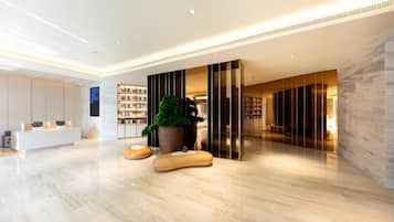 A modern lobby with a reception desk, a large potted plant, and a seating area with a view of the interior.