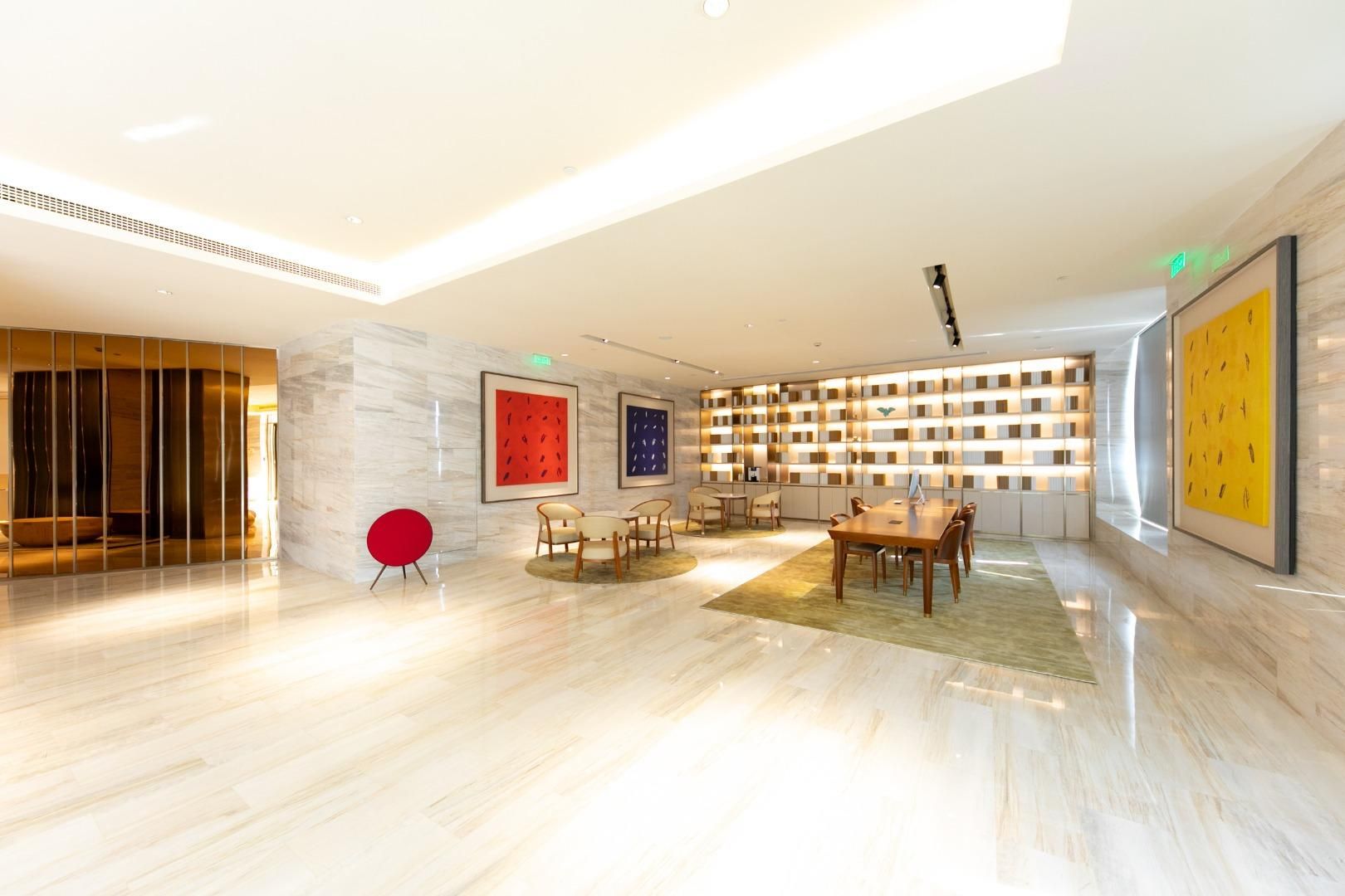 A spacious lobby with a modern design, featuring a seating area with chairs and a table, a large bookshelf, and a red accent chair.