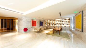 A spacious lobby with a modern design, featuring a seating area with chairs and a table, a large bookshelf, and a red accent chair.