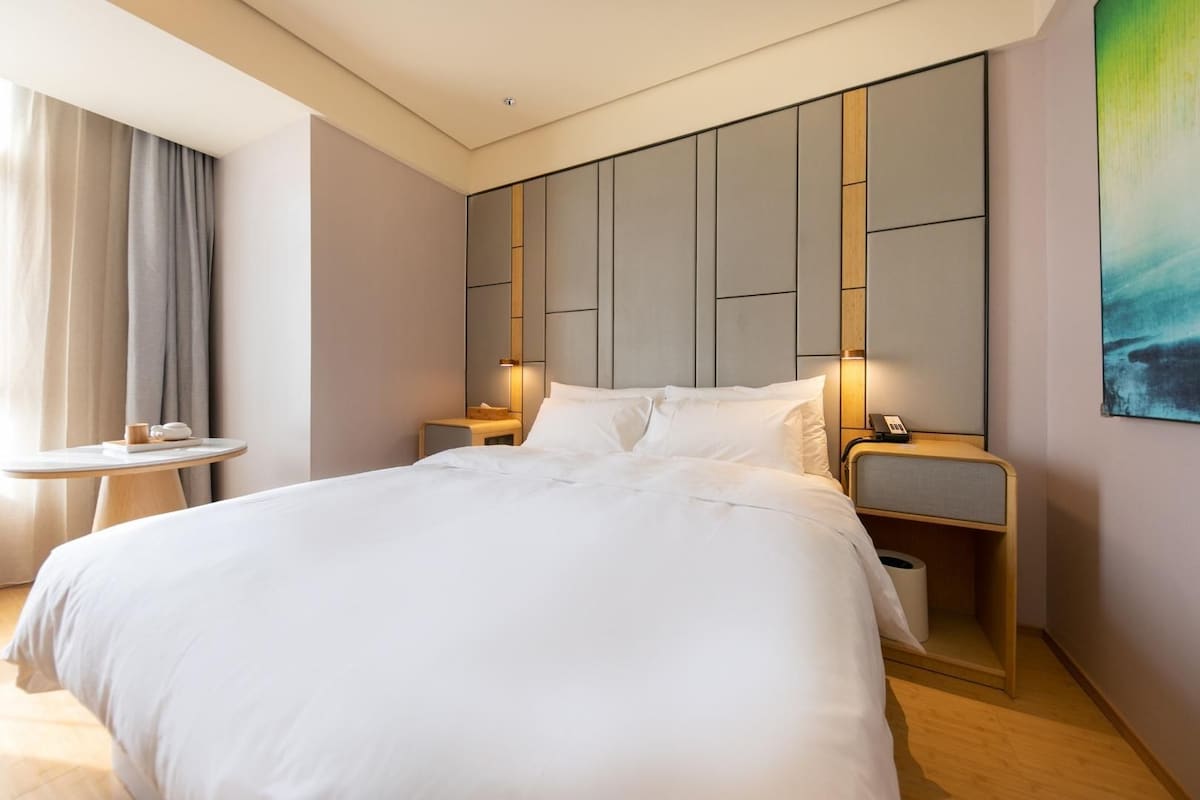 Una habitación de hotel moderna con una cama grande, mesitas de noche, una pequeña mesa redonda y un cuadro en la pared.
