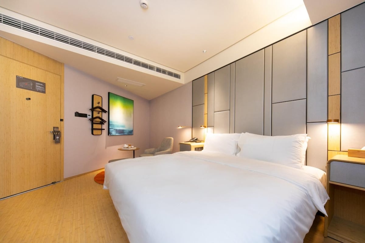 Habitación de hotel con una cama grande, una silla, una mesita pequeña y una obra de arte colgada en la pared.