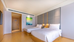 A hotel room with two beds, a painting on the wall, and a door leading to another room.
