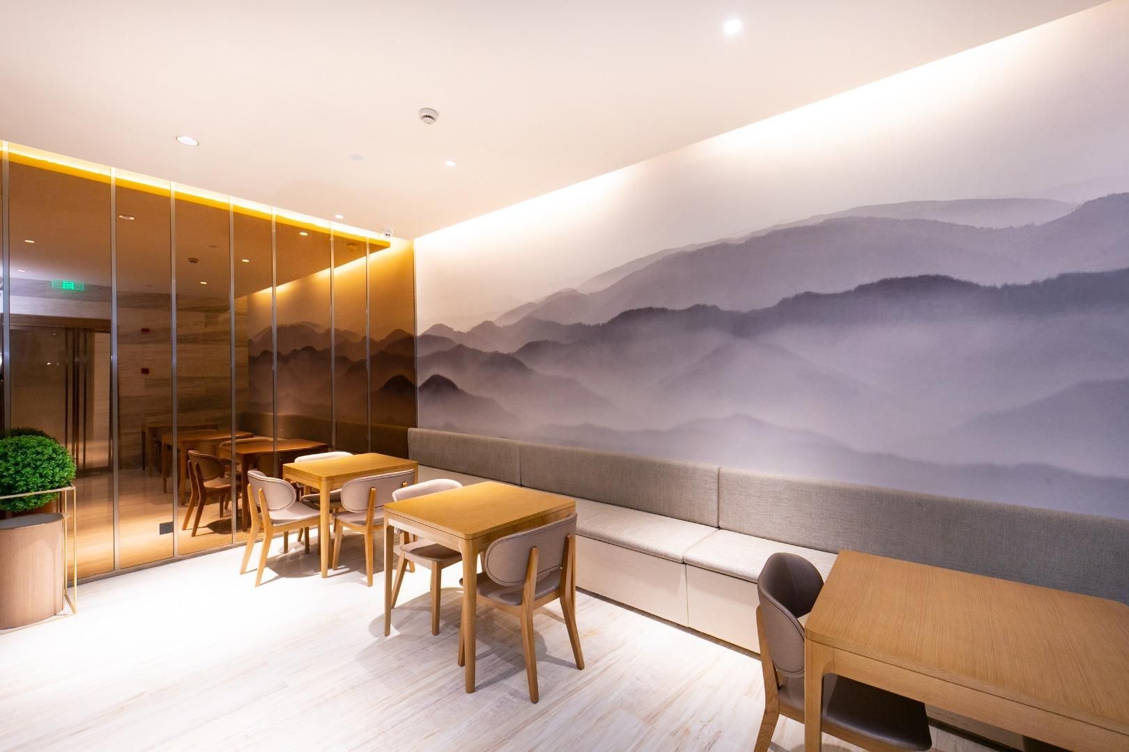 A modern interior with wooden tables and chairs, a glass partition, and a mural of mountains.