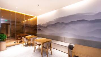 A modern interior with wooden tables and chairs, a glass partition, and a mural of mountains.
