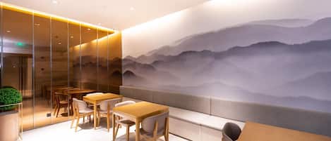 Un interior moderno con mesas y sillas de madera, un separador de vidrio y un mural de montañas.