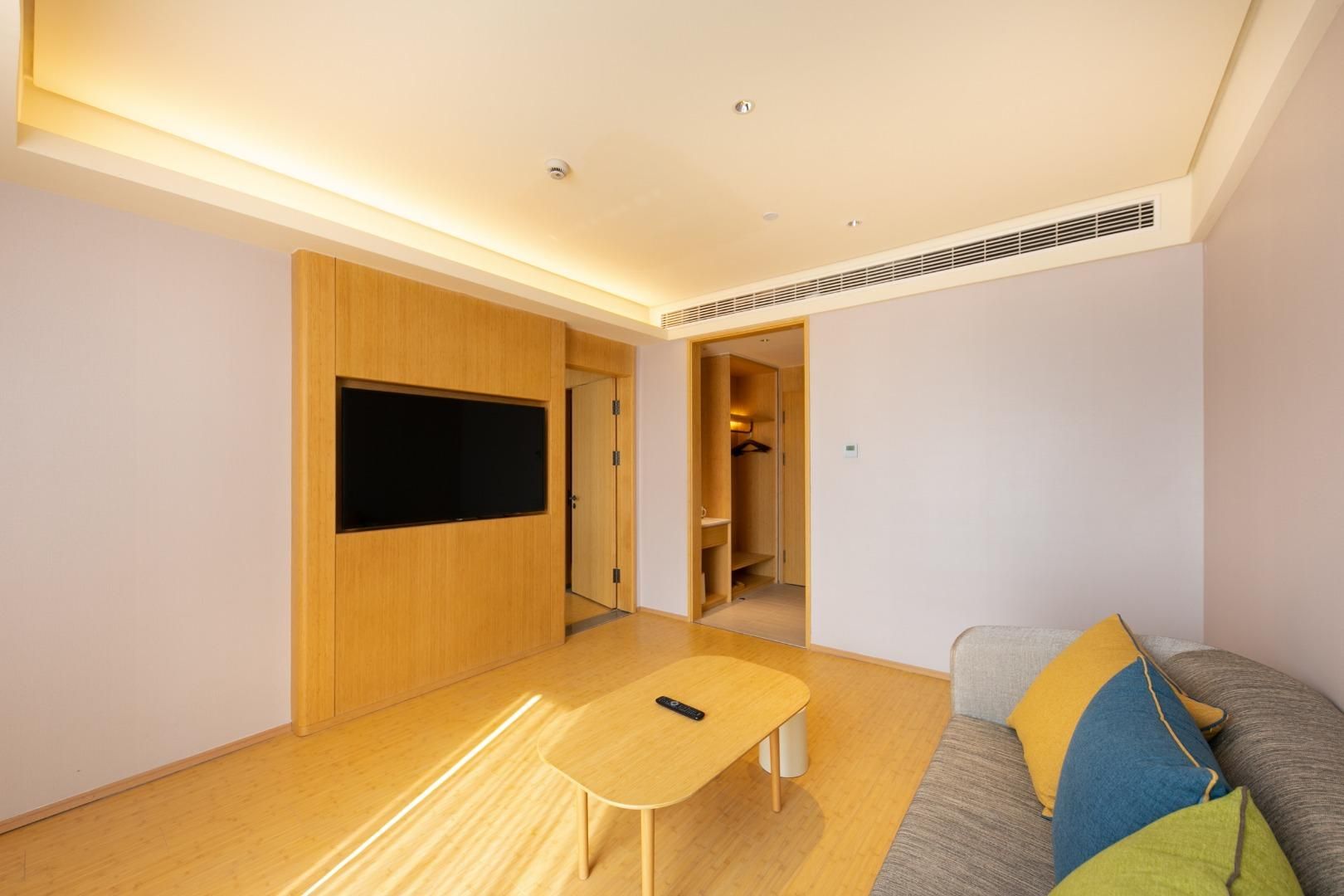 A modern living room with a flat-screen TV, a wooden table, a sofa with colorful cushions, and a walk-in closet.