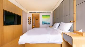 A modern hotel room with a large bed, a flat-screen TV mounted on the wall, a bedside table, and a painting on the wall.
