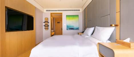 A modern hotel room with a large bed, a flat-screen TV mounted on the wall, a bedside table, and a painting on the wall.