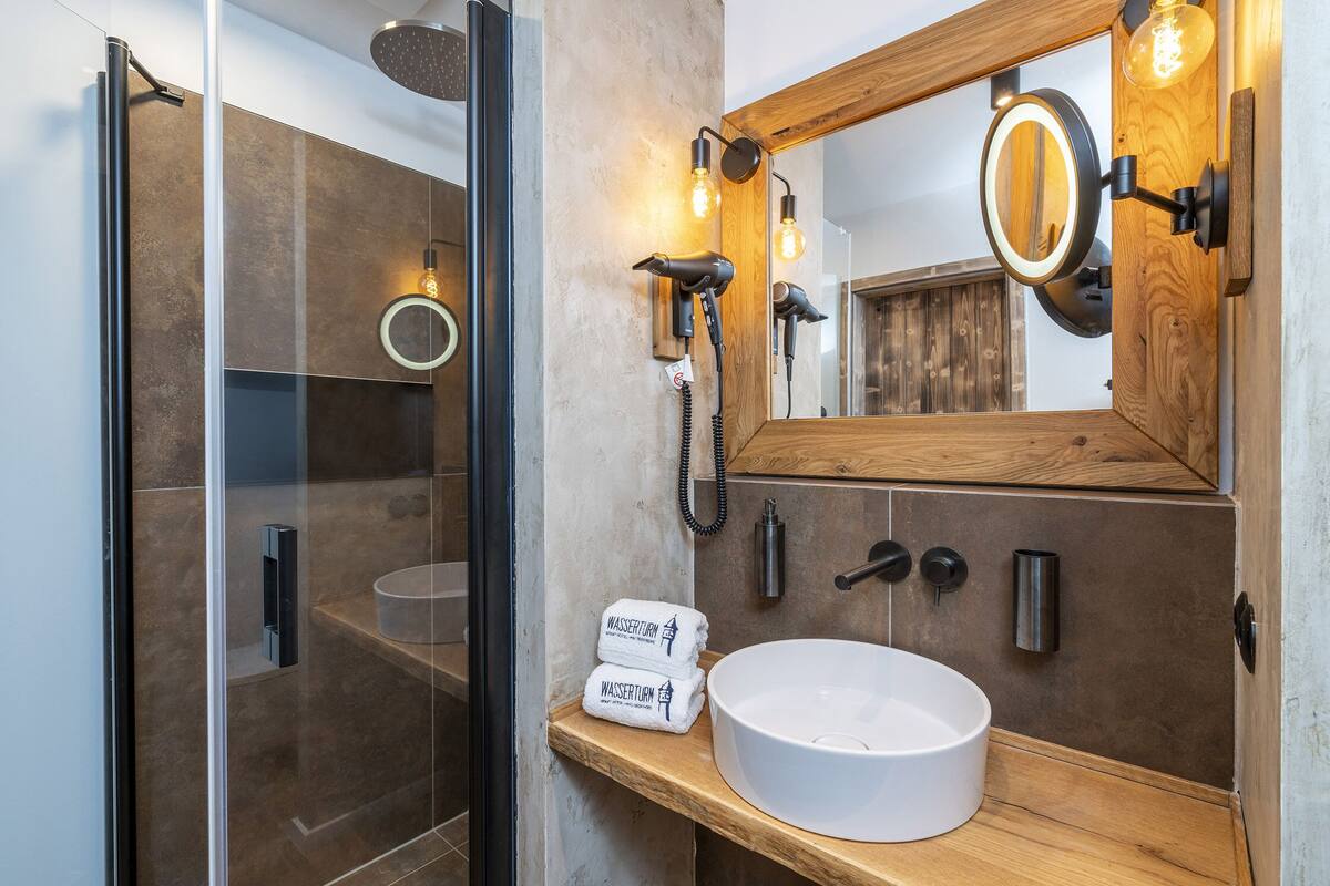 A modern bathroom with a glass shower enclosure, a wooden vanity with a white sink, and a large mirror with integrated lighting.