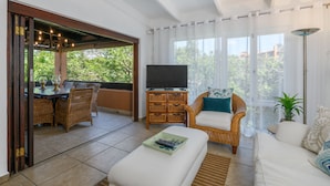 A spacious living area with a television, wicker furniture, and a balcony with a view of greenery. - San Lameer Villa Rentals 3115 (Southbroom)