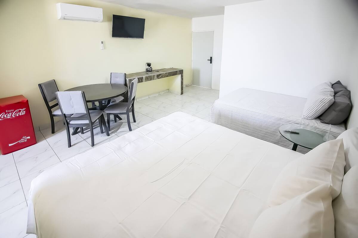 Ein Hotelzimmer mit Bett, Schreibtisch, Stuhl, einem kleinen Tisch und einem Fernseher.