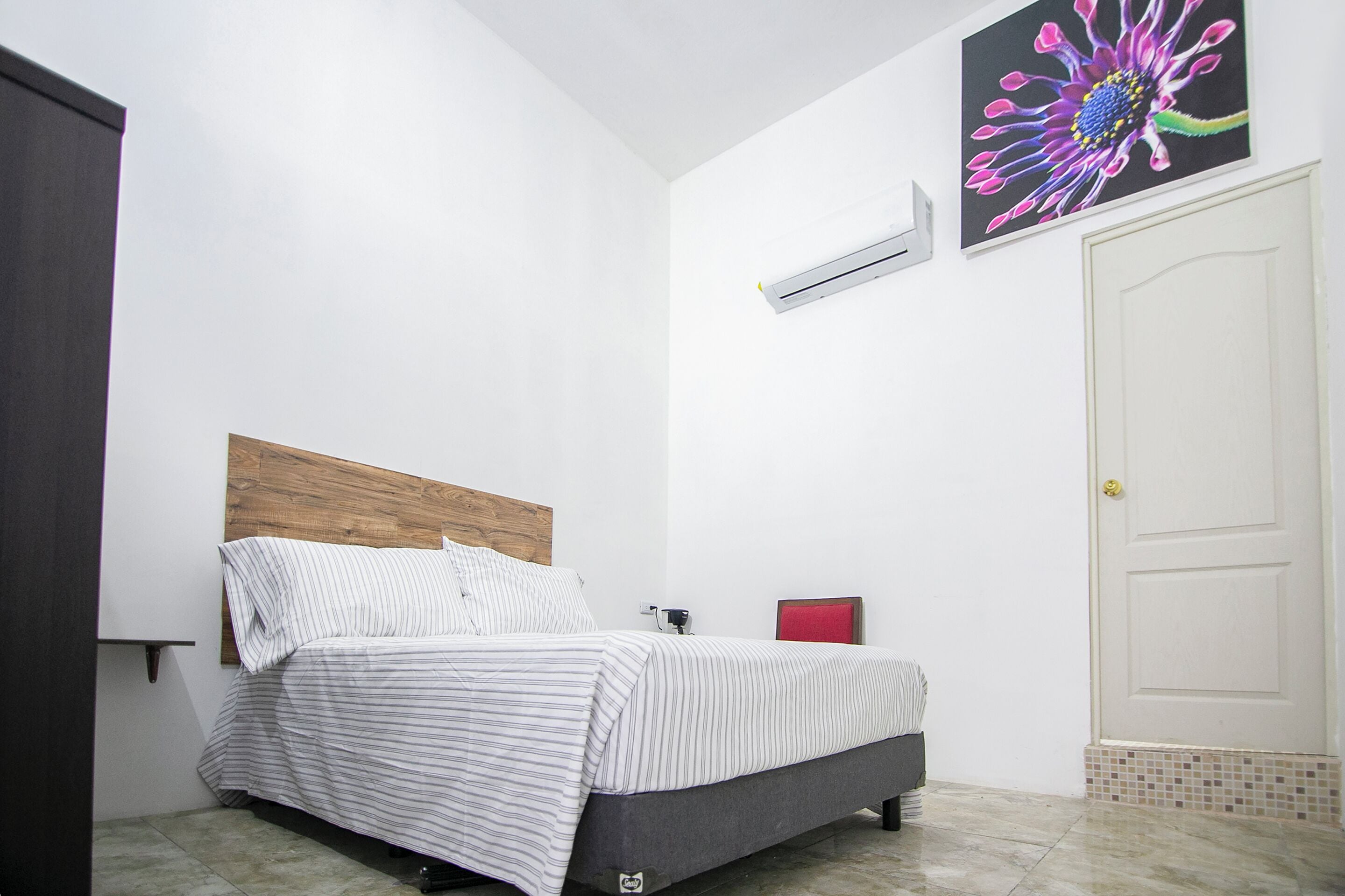 Un dormitorio con cama, cabecera, aire acondicionado, una puerta y una obra de arte en la pared.