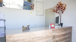 A reception desk with a wooden finish, a whiteboard with room rates, a potted plant, and a reflection of the room. - OYO Hotel Plaza Las Torres, Cabo San Lucas (Cabo San Lucas)