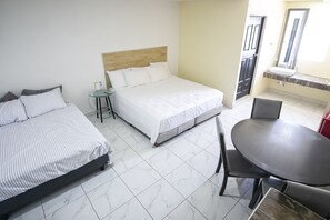 Ein Hotelzimmer mit zwei Betten, einem kleinen Tisch, einem runden Tisch und einem Badezimmer mit Waschbecken und Spiegel.