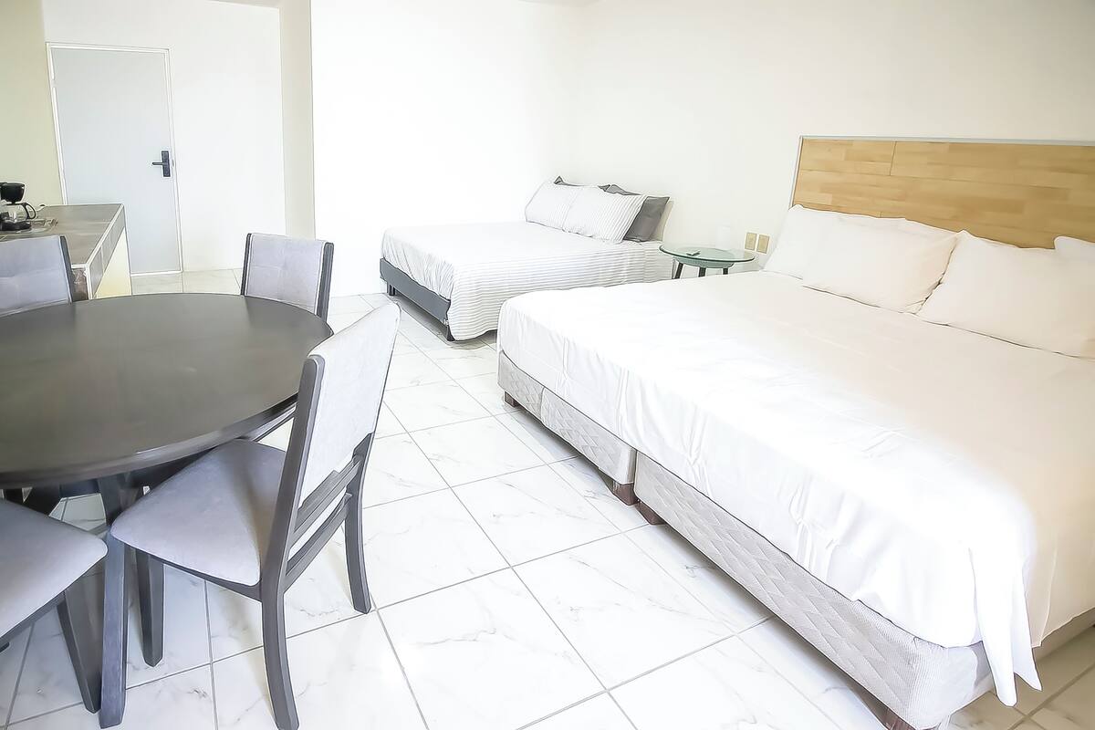 Ein Hotelzimmer mit zwei Betten, einem Esstisch mit Stühlen und einem kleinen Beistelltisch.