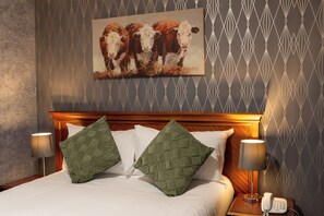 A hotel room with a bed, two green pillows, a painting of cows on the wall, and a bedside telephone. - Grampian Hotel (Perth)
