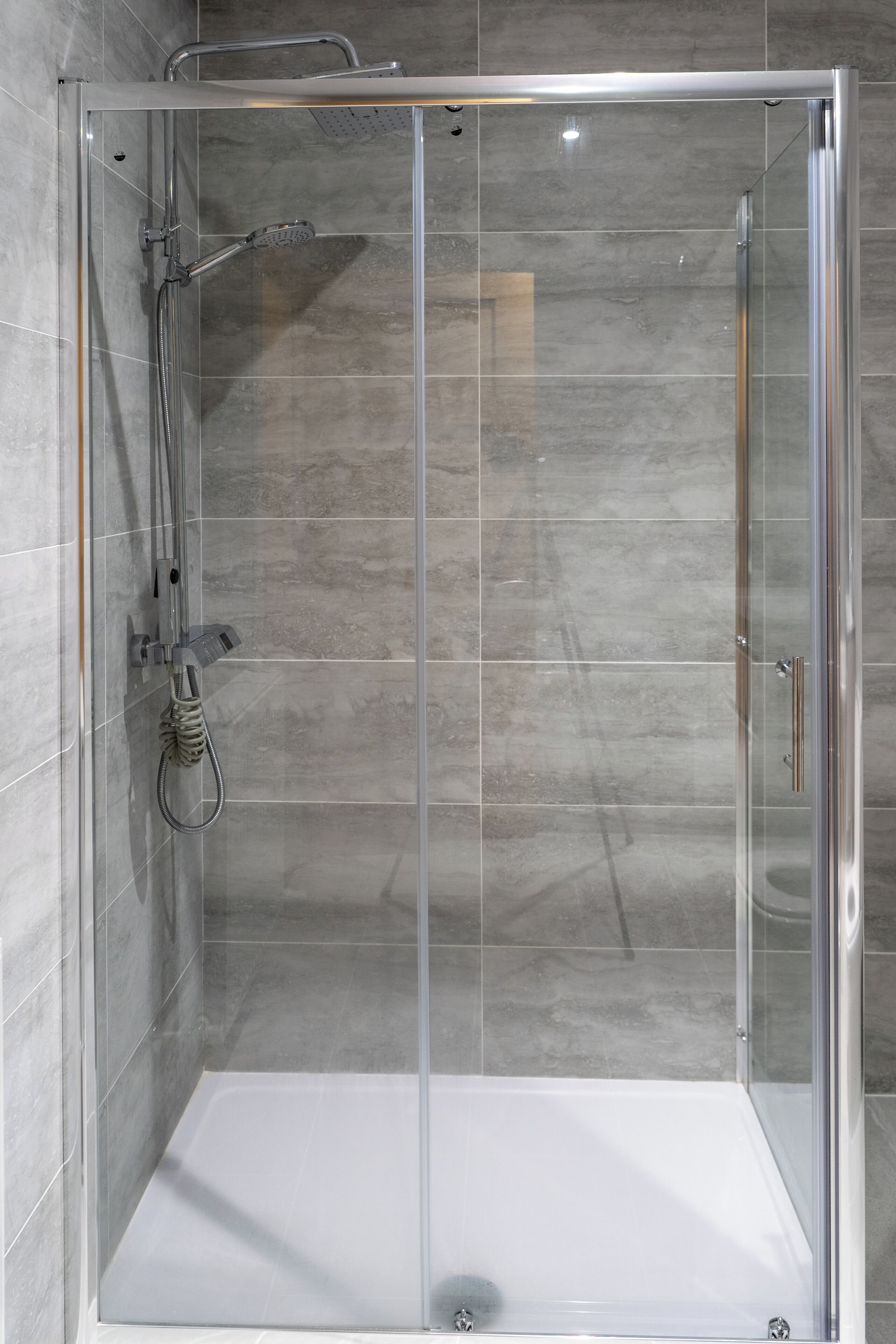 A clear glass shower enclosure with a handheld showerhead and a wall-mounted faucet.