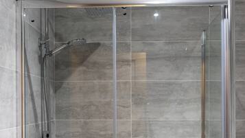 A clear glass shower enclosure with a handheld showerhead and a wall-mounted faucet.