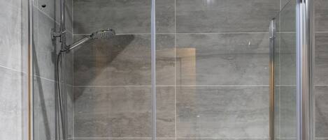 A clear glass shower enclosure with a handheld showerhead and a wall-mounted faucet.