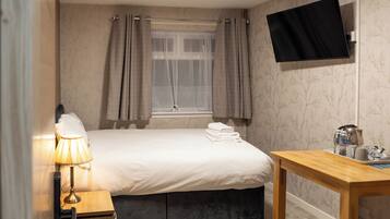 A hotel room with a bed, a bedside table with a lamp, a TV mounted on the wall, and a window with curtains.