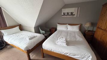 A room with two wooden beds, a chair, a nightstand, a lamp, and a cabinet.