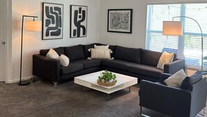 Una sala de estar moderna con un sofá seccional negro, una mesa de centro blanca y arte abstracto en las paredes.