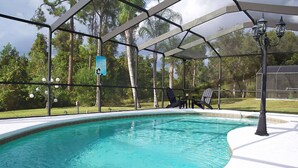 Una piscina con zona cubierta, rodeada de árboles y césped.