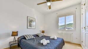 Une chambre à coucher avec un grand lit, deux lampes de chevet, un ventilateur de plafond, une fenêtre avec vue et un radiateur.