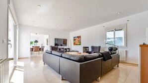 Un salon moderne doté d’un grand canapé en forme de L, d’un téléviseur à écran plat et d’un coin repas avec une table et des chaises.