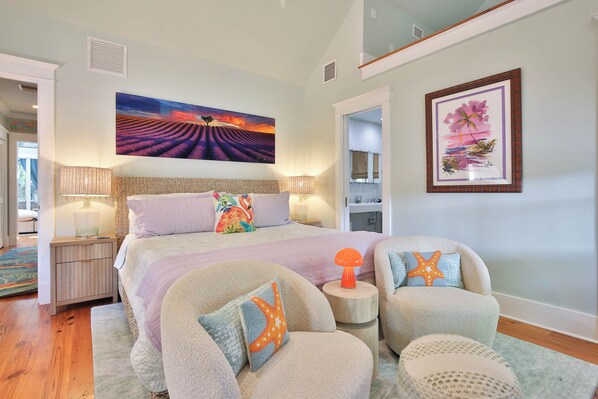 A bedroom with a large bed, two chairs, a nightstand, a painting, and a framed picture on the wall.