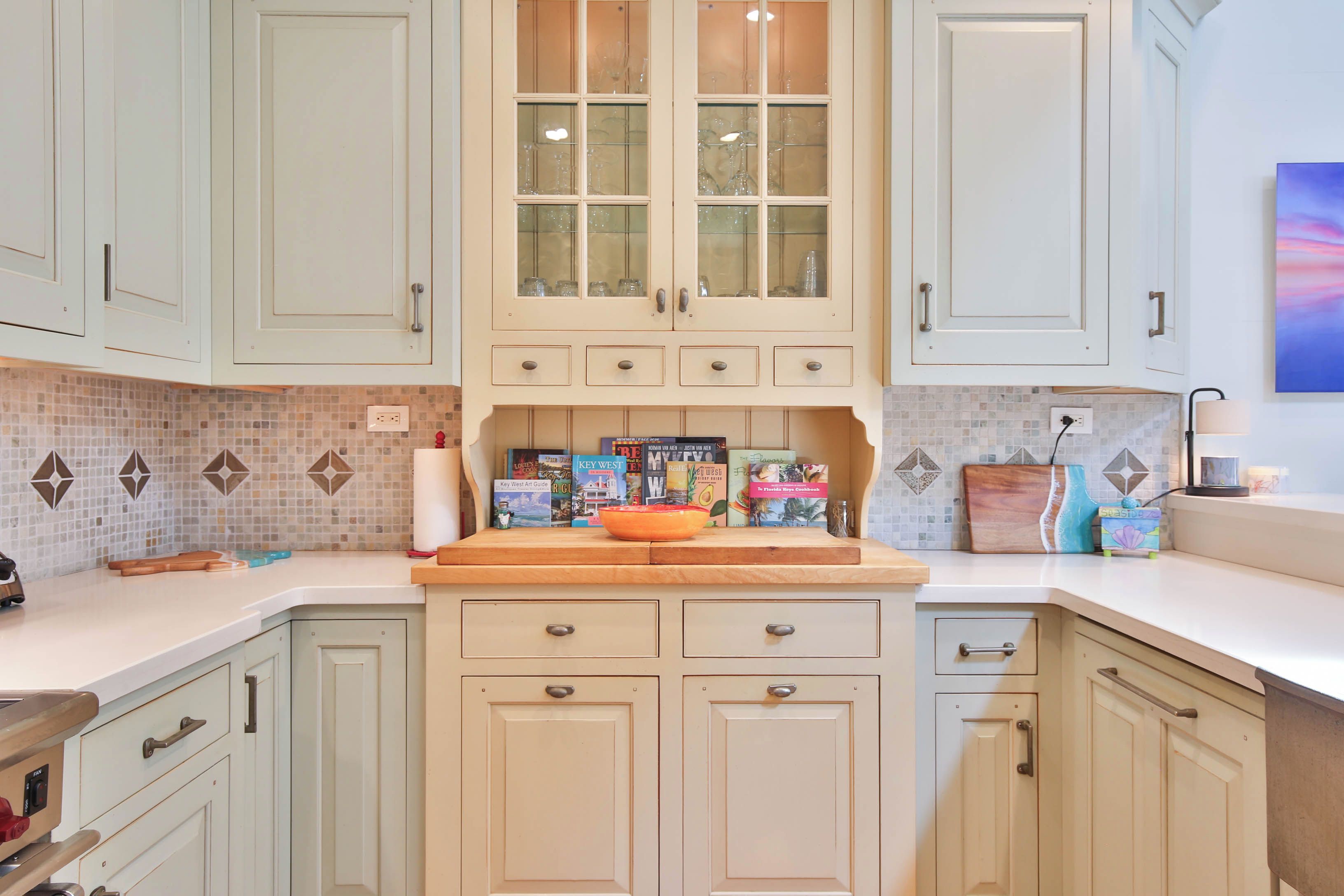 A kitchen with light-colored cabinets, a central island with a bowl, and a tiled backsplash.