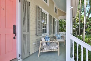 A porch with a bench and a table, a pink door, and a white railing.