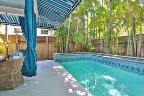 A swimming pool with a tiled edge, surrounded by a wooden deck and a bamboo fence.