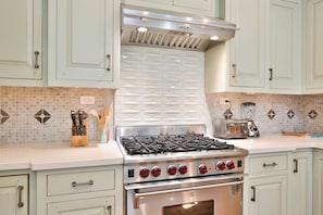 A kitchen with light-colored cabinets, a Wolf gas range, a Philips toaster, and a blender.