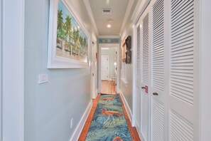 A hallway with a wooden floor, a painting on the wall, and a door with a fire exit sign. - LOVE LANDING ~ Charming 3 Bedroom, 3 Bathroom Home w/ Pool and Parking! (Key West)
