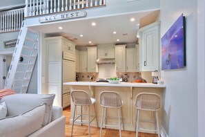 A kitchen with white cabinets, a central island with bar stools, and a staircase with a 'KEY WEST' sign.