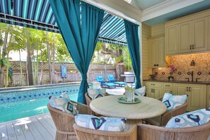 A poolside area with wicker furniture, a tiki bar sign, and a kitchen with a tiled backsplash. - LOVE LANDING ~ Charming 3 Bedroom, 3 Bathroom Home w/ Pool and Parking! (Key West)