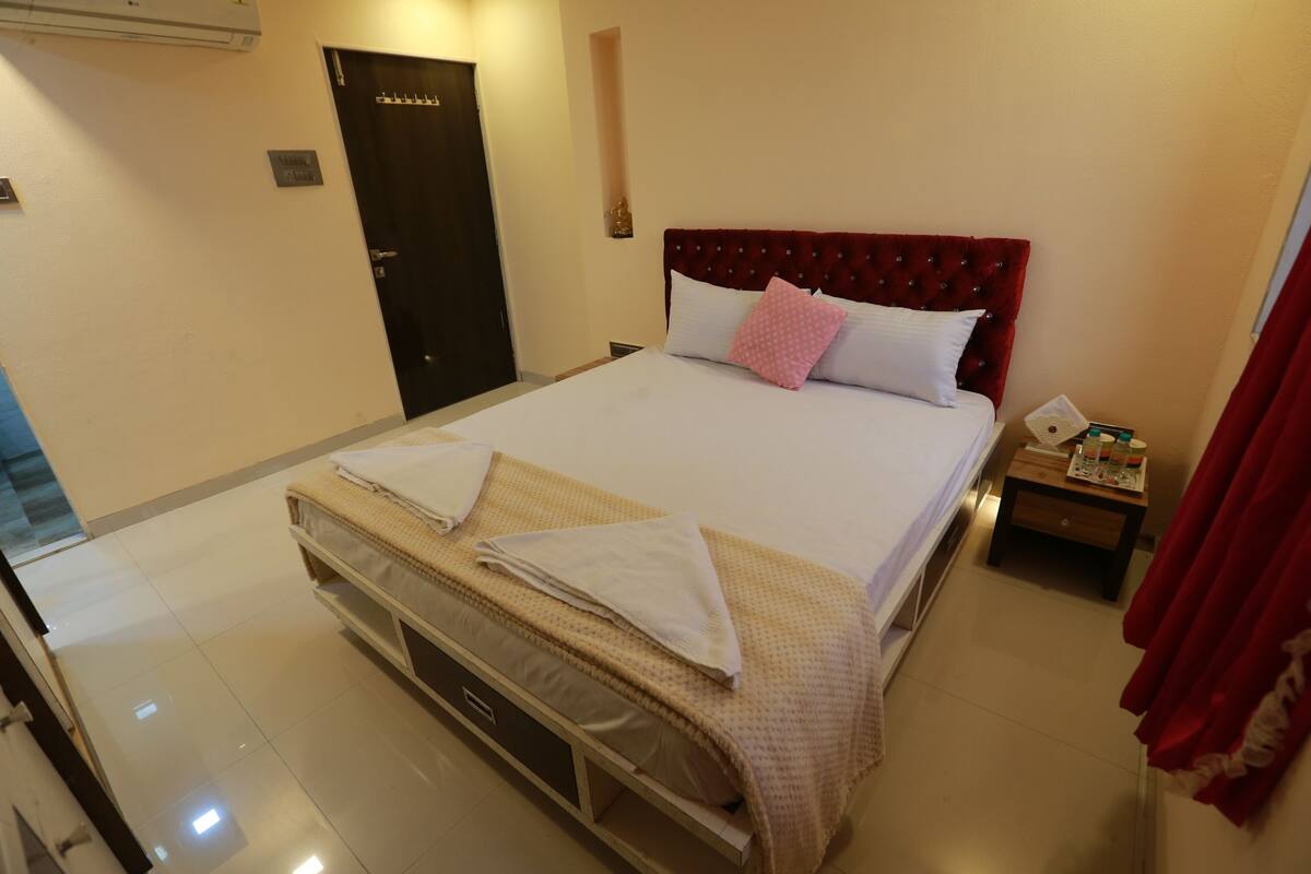 Una habitación de hotel con una cama grande, una mesita de noche con lámpara y una puerta.