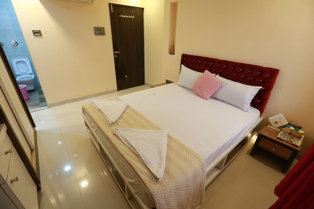 Una habitación de hotel con una cama, una mesita de noche de madera, un cabecero rojo y una puerta al baño.