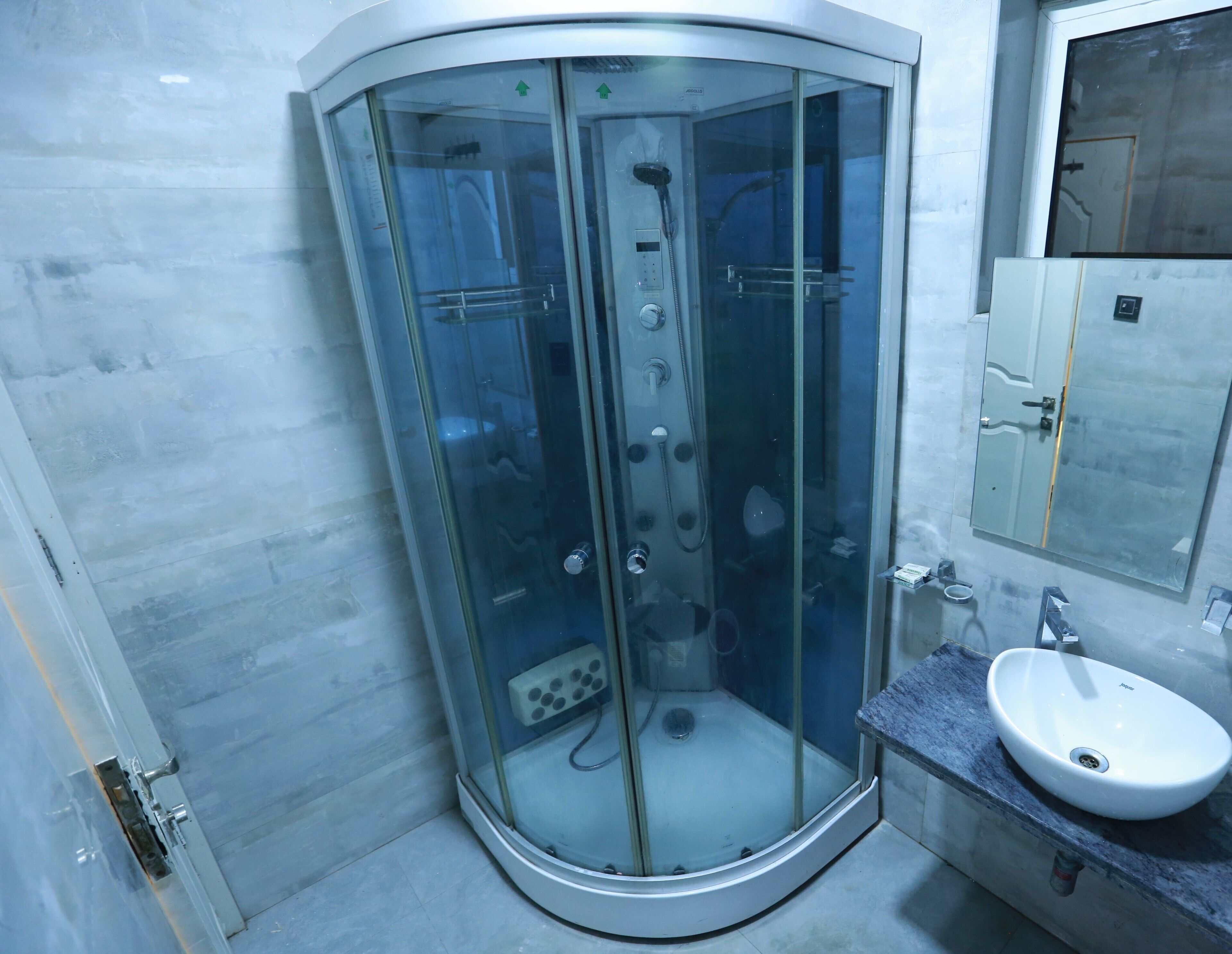 A corner shower enclosure with a glass door, a sink with a mirror, and a cabinet with a door.
