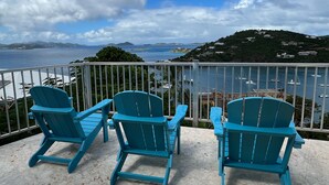 Una terrazza con tre poltrone Adirondack blu, un parapetto bianco e vista sul mare e colline in lontananza.