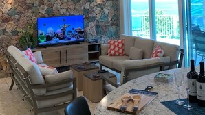 Un soggiorno moderno con una parete in pietra, una grande TV, posti a sedere confortevoli e vista sull'oceano.