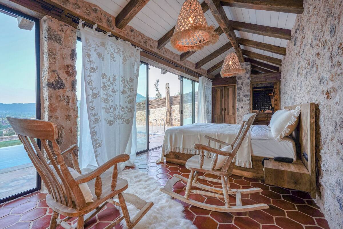 Une chambre à coucher rustique avec un lit, des fauteuils à bascule et une vue sur l’extérieur.