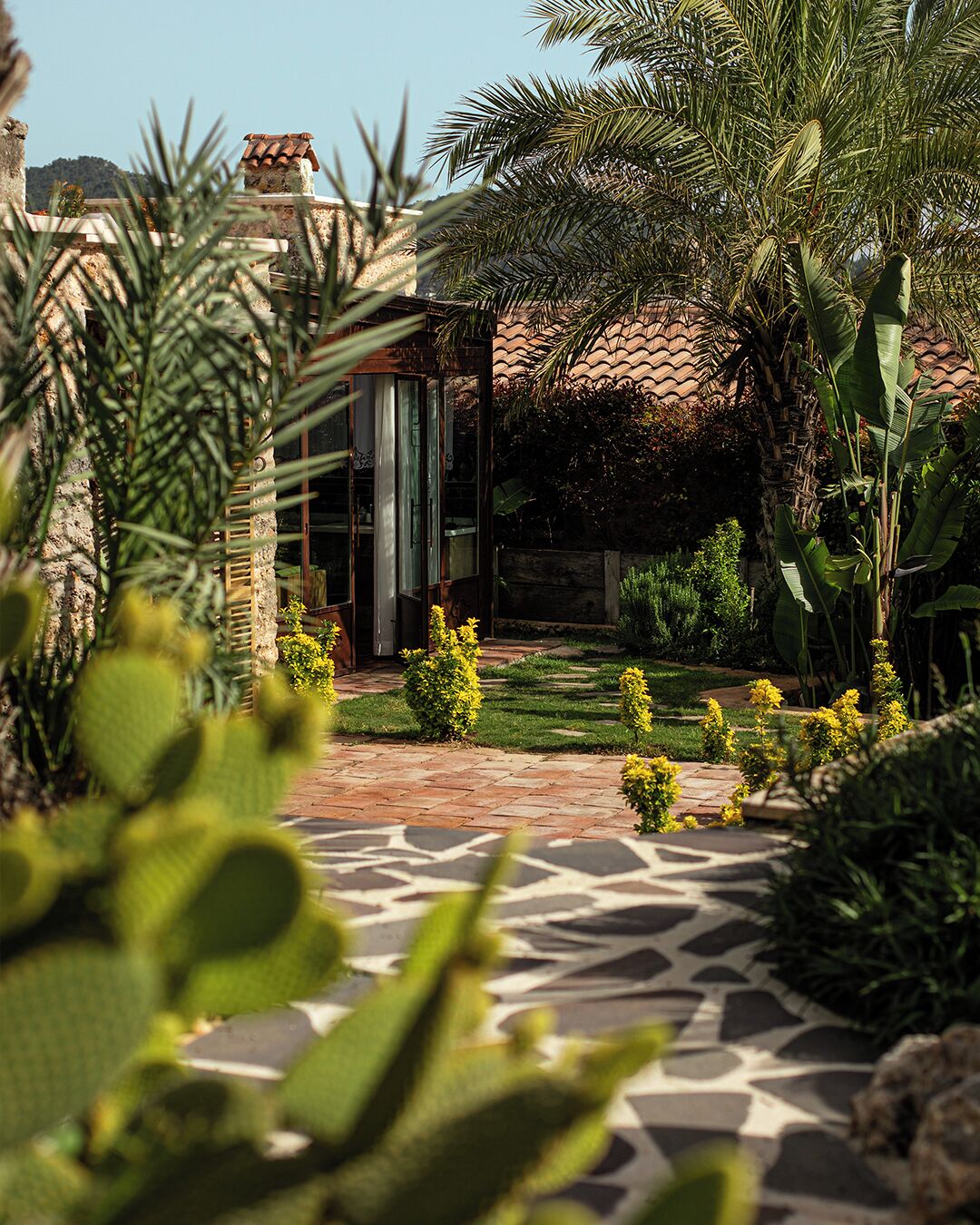 A garden pathway leading to a building with a tiled roof, surrounded by various plants and shrubs.