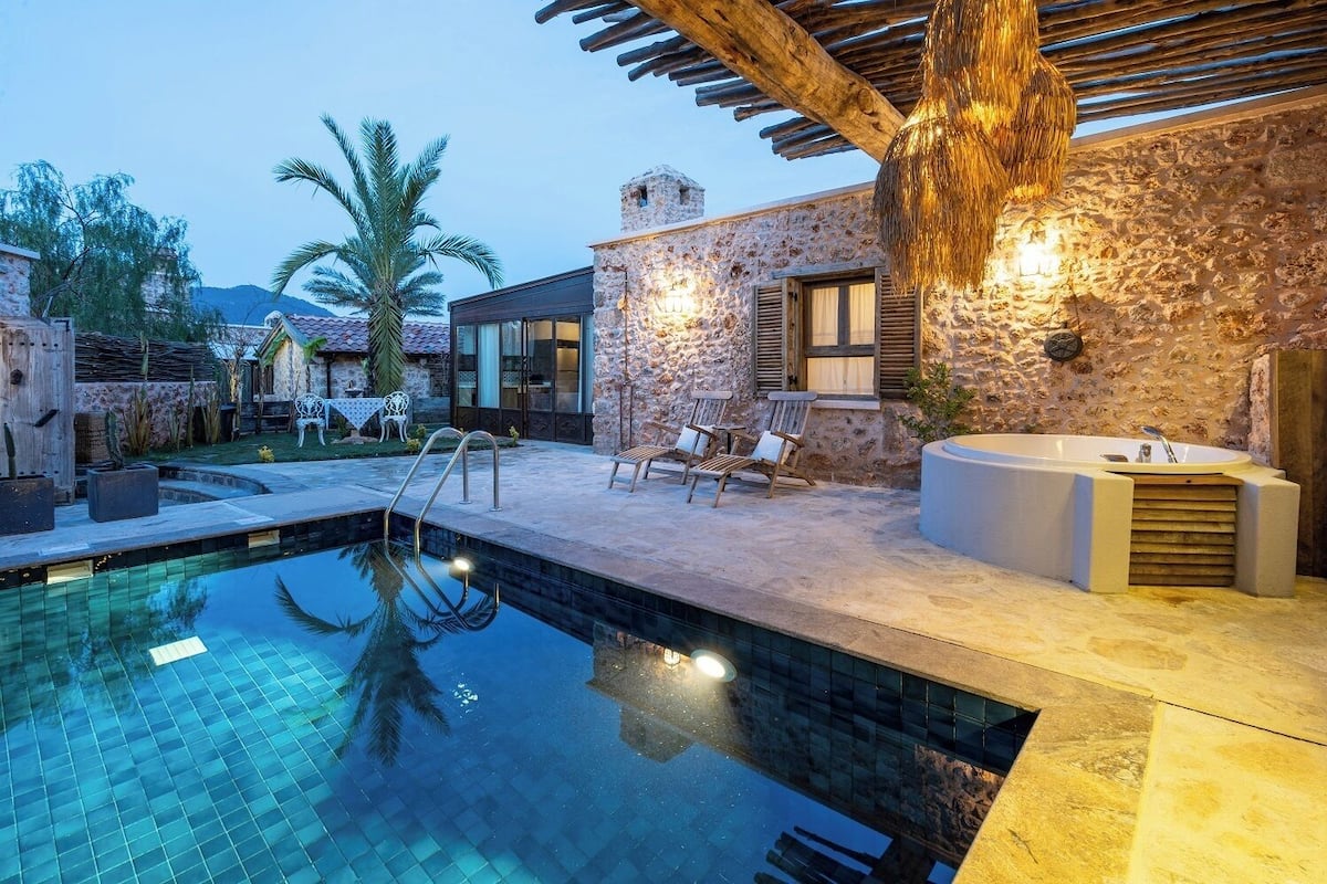 Un espace piscine agrémenté d’un mur en pierre, d’une terrasse en bois et d’un jacuzzi.