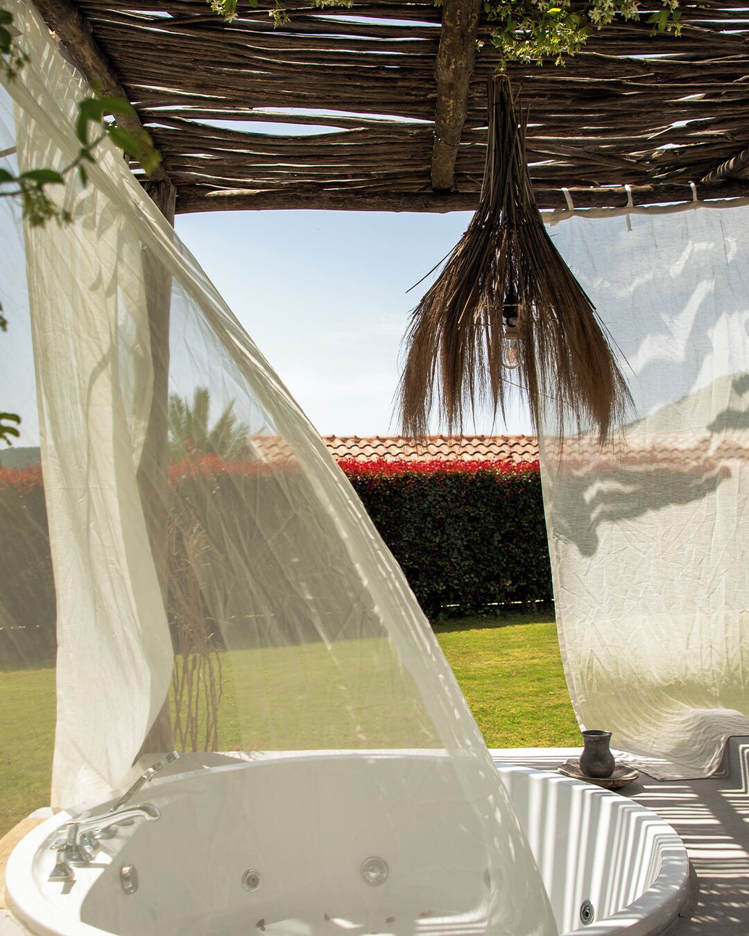 A hot tub under a pergola with a view of a garden and a hedge.