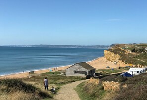 A coastal landscape with a beach, a small wooden structure, and a path leading down to the beach.